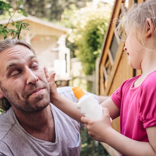 Daughter putting suncream on her father's face in the garden