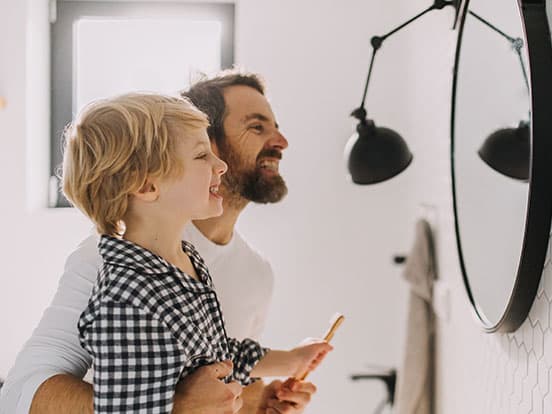 Father and son brushing together at bathroom mirror
