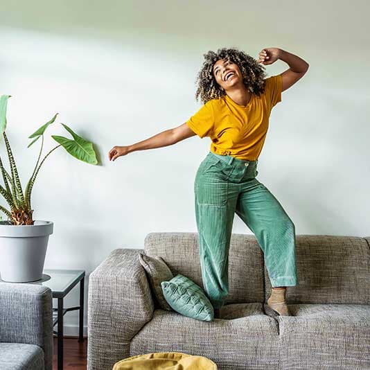 Happy healthy lady dancing on sofa at home