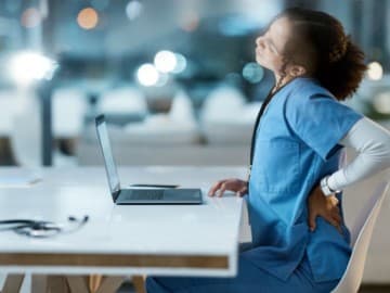 Medical professional stretching whilst sitting down by a desk with laptop
