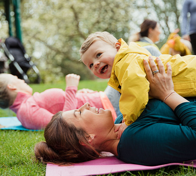 Woman holding her baby whilst taking part in outdoor yoga