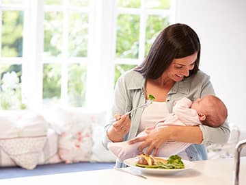 New mum eating health meal while holding baby