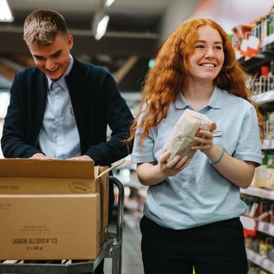 Two grocery store employees smiling whilst re-stocking shelves