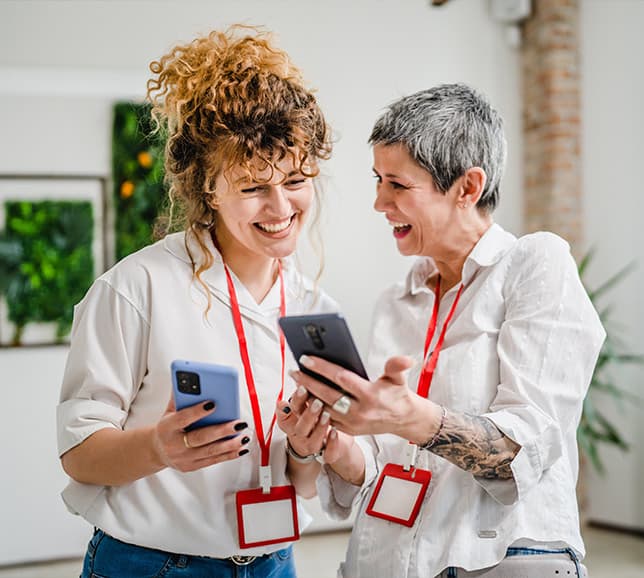 Two women smiling at phones at work