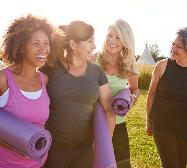 A group of women smiling and walking with yoga mats